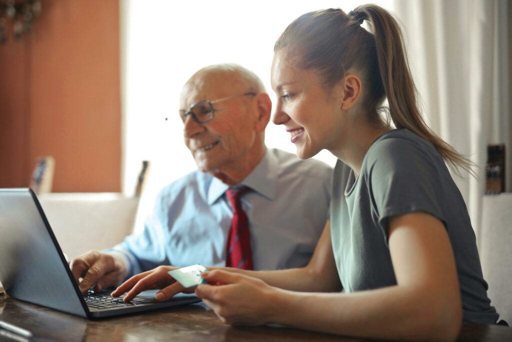 Senior man and daughter sitting at a table and looking at a computer.